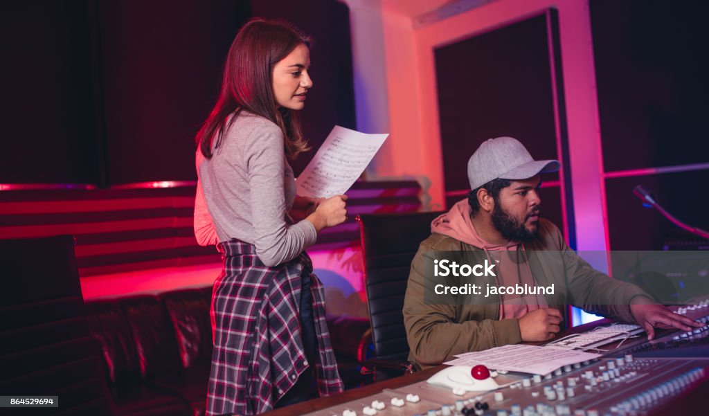 Sound engineers working in music recording studio Female singer with man working on audio mixing console in recording studio. People working in professional music studio. Recording Studio Stock Photo