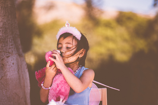 Little Asian girl dressed in fairy costume playing in garden and kissing stuffed toy animal