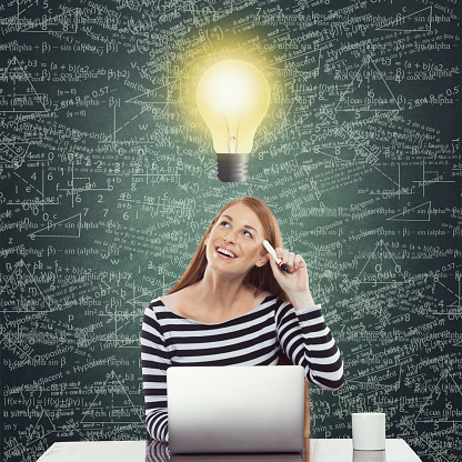 Confused businesswoman working on laptop under glowing lightbulb