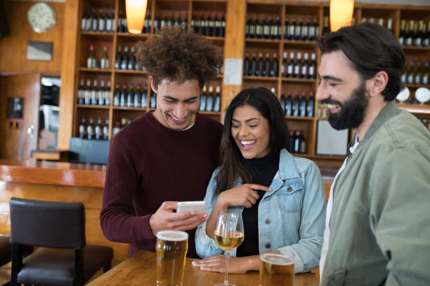 přátelé hledají své fotografie na mobilním telefonu v baru - barový pult fotky - stock snímky, obrázky a fotky