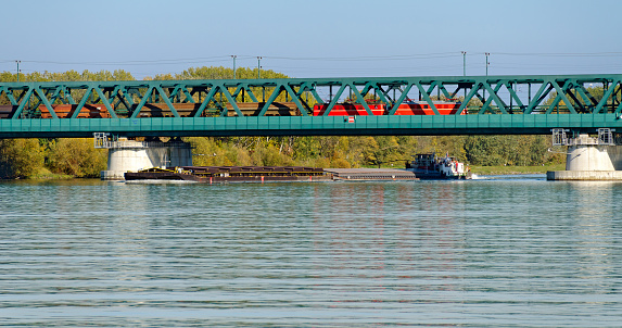 cargo vessel under a bridge with crossing cargo train on the river Danube at the city of Tulln, Austria
