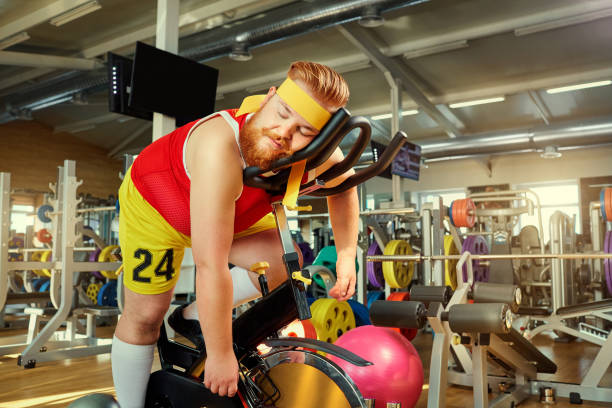 A fat man is tired on a simulator in the gym A fat man is tired on a simulator in the gym. exhaustion photos stock pictures, royalty-free photos & images