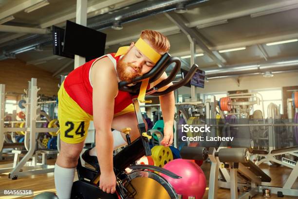 A Fat Man Is Tired On A Simulator In The Gym Stock Photo - Download Image Now - Humor, Sleeping, Exercising