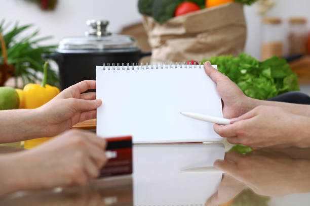 istock Close-up of human hands pointing into note book copy space area in the kitchen.  So much ideas for tasty cooking. Vegetarian, healthy meal and friendship concept 864569212
