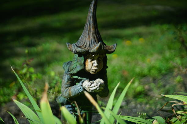 Small dwarf decorates the garden. figure for beauty of a house, park. The elf gathers dew in her palms. Beanie bell. Porcelain ceramic toy, realistic shape, Standing on the lawn near long grass blades