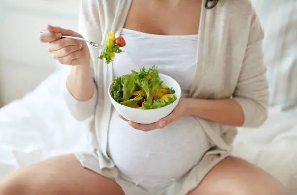 Photo of close up of pregnant woman eating salad at home