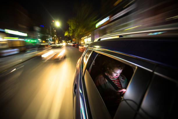 Woman in Rear of Car Driving Through New York City A woman sits in the back of a car, possibly a rideshare, looking at her mobile phone. The lights of New York City streak past. crowdsourced taxi stock pictures, royalty-free photos & images