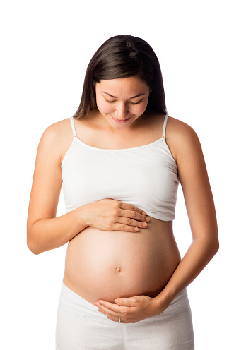 A beautiful latin pregnant woman standing, holding belly and smiling.