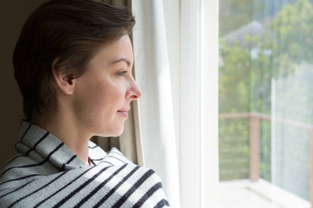 istock Woman looking through a window at home 864586774