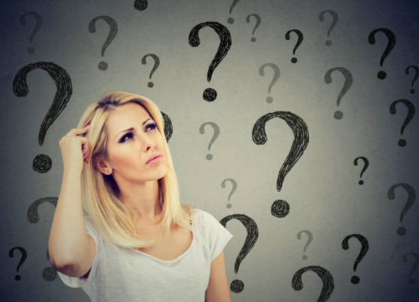 istock Portrait confused thinking woman bewildered scratching head seeks a solution looking up at many question marks isolated on gray wall background. Human face expression 864588970