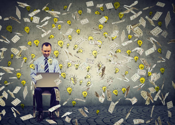 istock Mature man using a laptop building online business dollar bills and light bulbs falling down. Money rain IT entrepreneur success economy concept 864589818