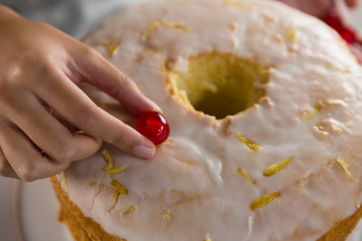 Close-up of woman toping a fresh baked cake with cherry