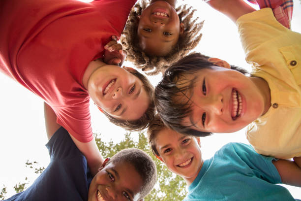 Multi-ethnic group of school children playing on school playground. Multi-ethnic group of school children playing on school playground.  The group of friends huddle up to plan their next adventure.  Education in USA, exercise themes. mixed age range stock pictures, royalty-free photos & images