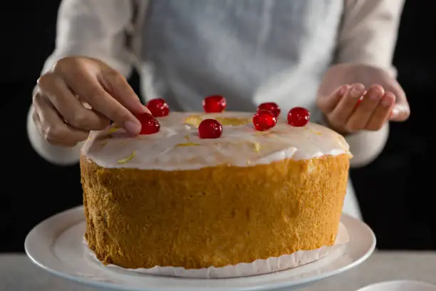 Photo of Woman toping a fresh baked cake with cherry