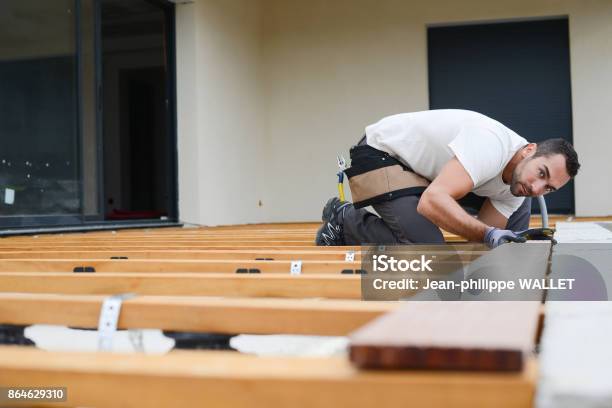 Handsome Young Man Carpenter Installing A Wood Floor Outdoor Terrace In New House Construction Site Stock Photo - Download Image Now