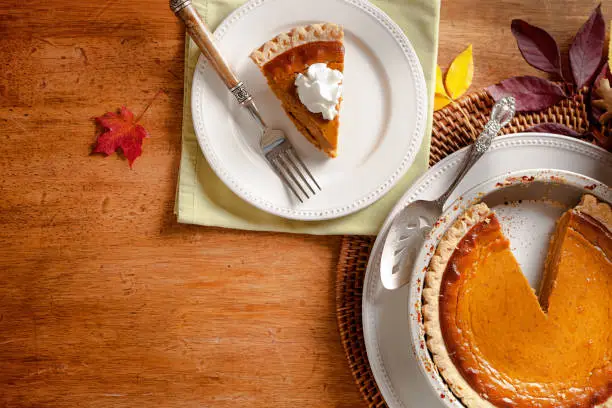 Still life of a autumn scene, with pumpkin pie for the traditional Thanksgiving dinner. A slice of pie is served with whipped cream.
