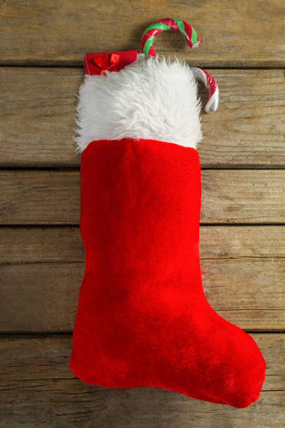 istock Wrapped gift box and candy cane in stocking against wooden wall 864644528