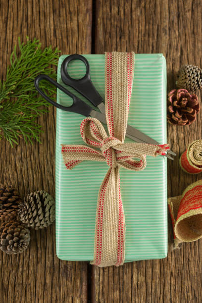 istock Scissors, pine cones, leaves and ribbon with wrapped gift box on wooden table 864644840
