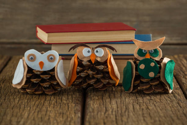 istock Owl decorated with pine cone and book stack on wooden table 864648308
