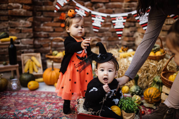 彼の後ろに立っている彼の妹とかぼちゃのカートに座っている赤ちゃん - child party group of people little girls ストックフォトと画像