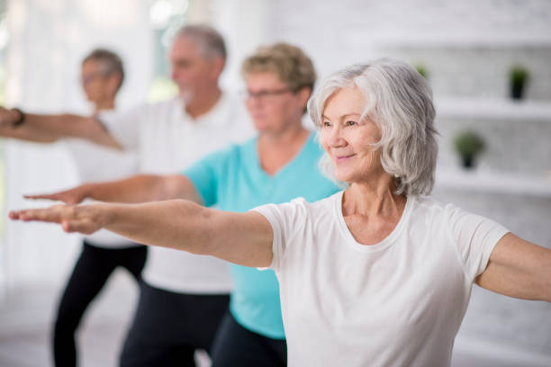 Reaching Out A multi-ethnic group of adult men and women are indoors in a fitness studio. They are wearing casual clothing while at a yoga class. A senior Caucasian woman is smiling while stretching out her arms. exercise class stock pictures, royalty-free photos & images