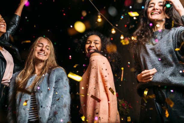 istock Female friends dancing under confetti at night, looking at camera 864661810
