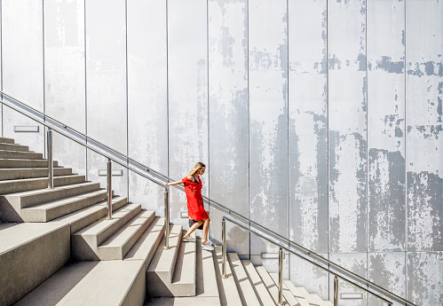 Business woman in red dress on the big stairway on the grey wall background