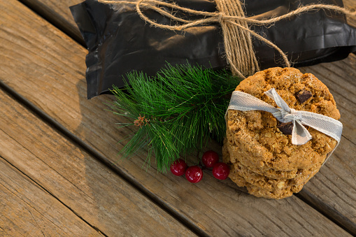 High angle view of cookies with pine needles and cheeries by plastic bag on wooden table