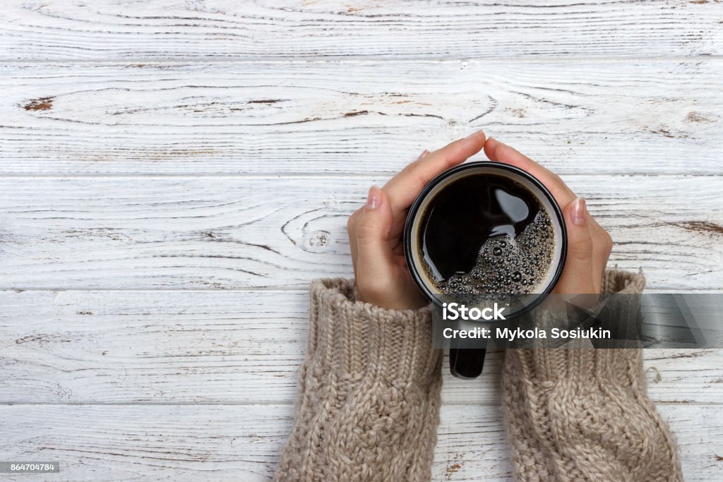 Donna che tiene tazza di caffè caldo su tavolo rustico in legno, foto ravvicinata delle mani in maglione caldo con tazza, concetto di mattina d'inverno, vista dall'alto - Foto stock royalty-free di Caffè - Bevanda