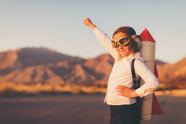 Young Business Girl with Rocket Pack A young girl businesswoman or student dressed in business attire looks to the distance while wearing a rocket strapped to her back and a flying cap and goggles. She is standing on a country road among the mountains of Utah, USA. She is confident in her abilities to lead her business and obtain her goals. child strength stock pictures, royalty-free photos & images