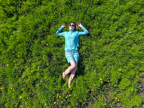 beautiful girl lying down of grass. The girl lies in a turquoise dress on the lawn.