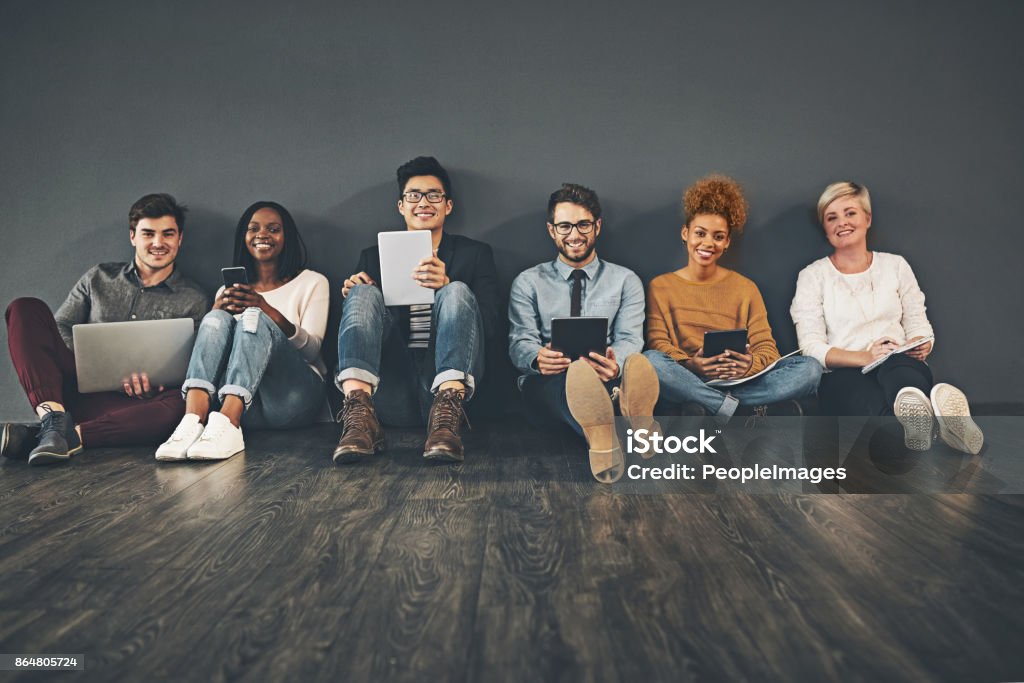 Lets sit down and get social Studio shot of a diverse group of creative employees social networking against a grey background Looking At Camera Stock Photo