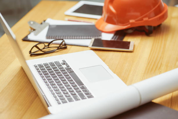 istock Laptop ,glasses, note book ,phone ,blueprint and orange safety helmet stacking on table at construction site for Engineer, foreman and worker , selective focusing . 864866150