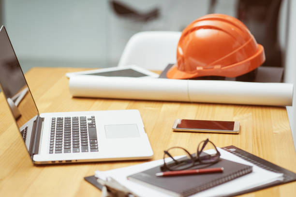 istock Laptop ,glasses, note book ,phone ,blueprint and orange safety helmet stacking on table at construction site for Engineer, foreman and worker , selective focusing . 864866154