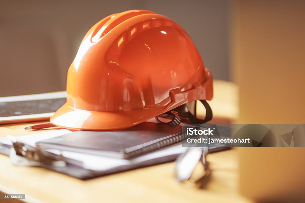 Laptop ,glasses, note book ,phone ,blueprint and orange safety helmet stacking on table at construction site for Engineer, foreman and worker , selective focusing . Occupational Safety And Health Stock Photo