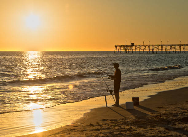 A surf fisherman enjoys a dramatic sunset on the shore of Caswell Beach, NC.