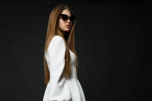 Stylish girl in a white dress and sunglasses on a black background