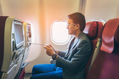 Young asian business man smiling and playing game with happinest in airplane