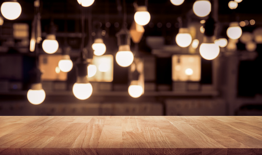 Wood table top on blurred of counter cafe shop with light bulb background.For montage product display or design key visual layout.Wood table top on blurred of counter cafe shop with light bulb background.For montage product display or design key visual layout.