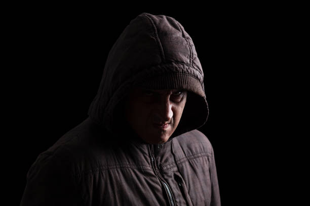 istock Man with repressed anger and violent instinct hiding in the shadows. Face partly hidden with hood, and standing in the darkness. 864915492