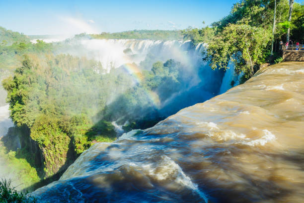 Puerto Iguazu: Tourists admiring the mighty Iguazu waterfalls, and a rainbow, in Iguazu National Park on the border of Argentina and Brazil. Argentinian side