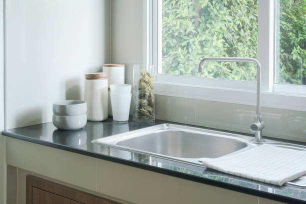 istock Kitchen sink next to window and white ceramicware on counter top 864925660