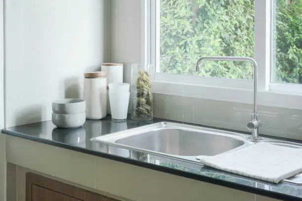 Kitchen sink next to window and white ceramicware on counter top
