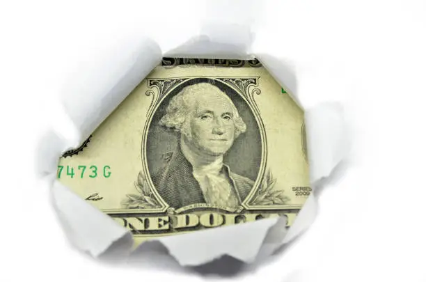 Photo of US currency macro peeking through torn white paper.