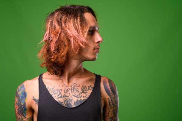 joven rebelde con tatuajes del cuerpo sobre fondo verde - tattoo men profile punk fotografías e imágenes de stock