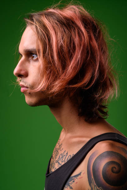 rebellious young man with body tattoos against green background - tattoo men profile punk imagens e fotografias de stock