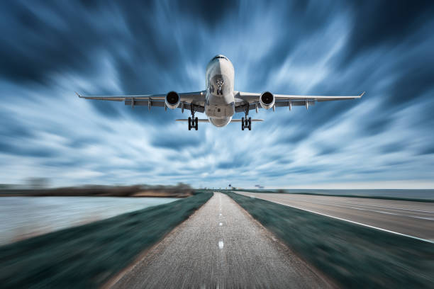istock Airplane and road with motion blur effect in overcast. Landscape with passenger airplane is flying over the asphalt road and cloudy sky. Commercial plane is landing. Aircraft with blurred background 864965766