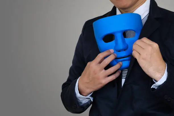 Businessman is hiding blue mask in your suit on gray background with clipping path and copy space