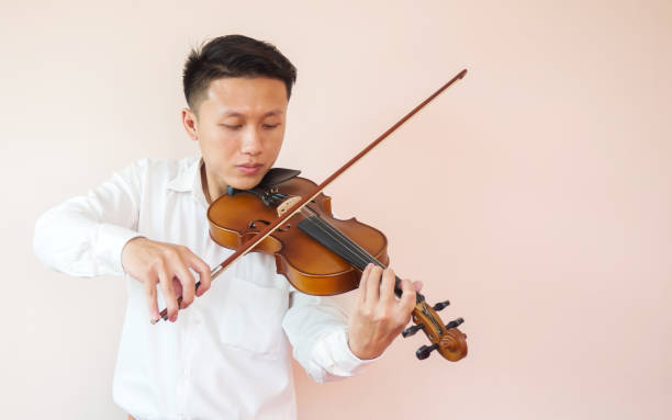 istock Young Asian man play violin. Classical music instrument. String equipment. Copy space and white in pink shade background. 864996584