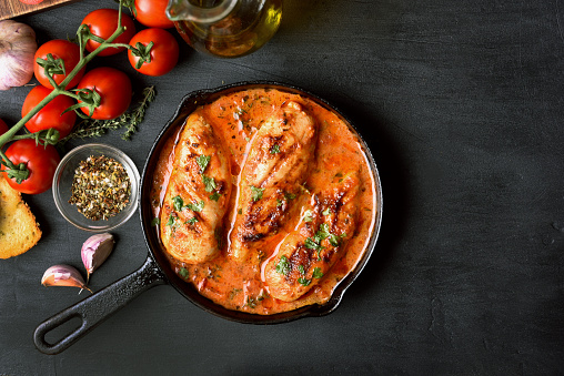 Stewed chicken breast with tomato sauce in frying pan on dark stone background with copy space, top view\